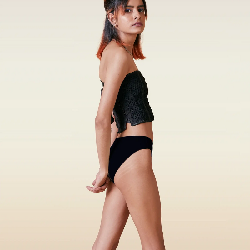 Woman wearing a black top and underwear on a beige background
