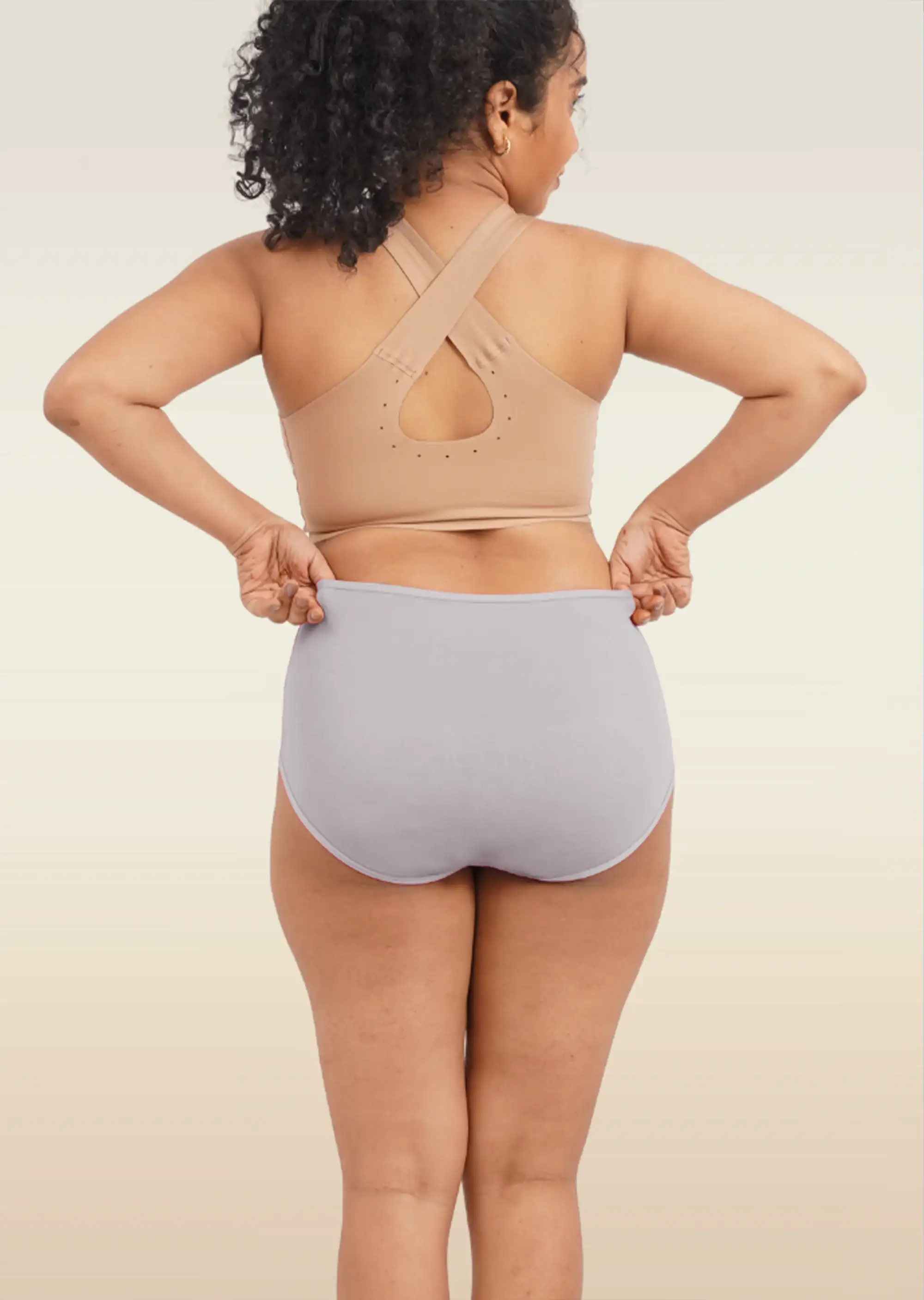 Person wearing a beige sports bra and light gray high-waisted underwear on a plain background