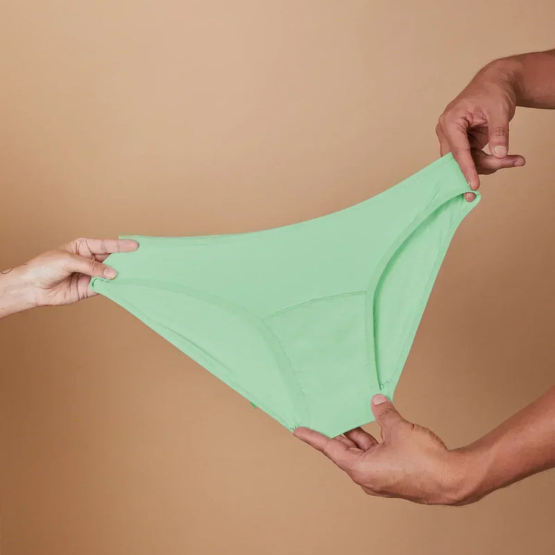 Green underwear held between two hands against a beige background
