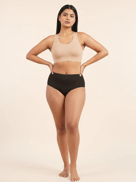Woman wearing a beige sports bra and black mid-waist underwear on a beige background
