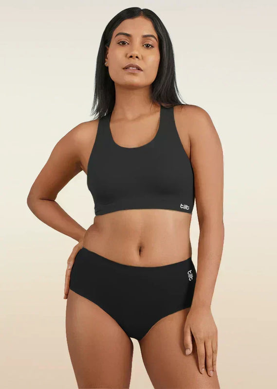 Woman wearing a black sports bra and mid-waist underwear on a beige background