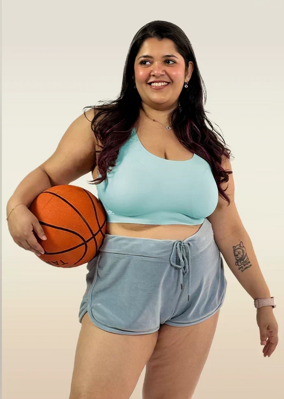 Woman holding a basketball wearing a  blue bra and gray shorts on a plain background