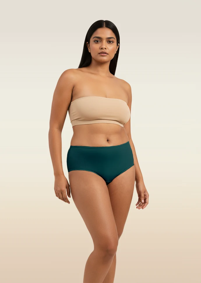 Woman wearing a beige strapless top and teal mid-waist underwear on a beige background