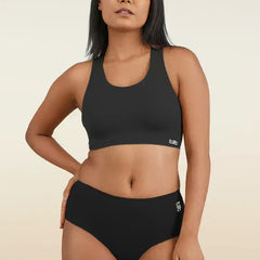 Woman wearing a black sports bra and mid-waist underwear on a beige background