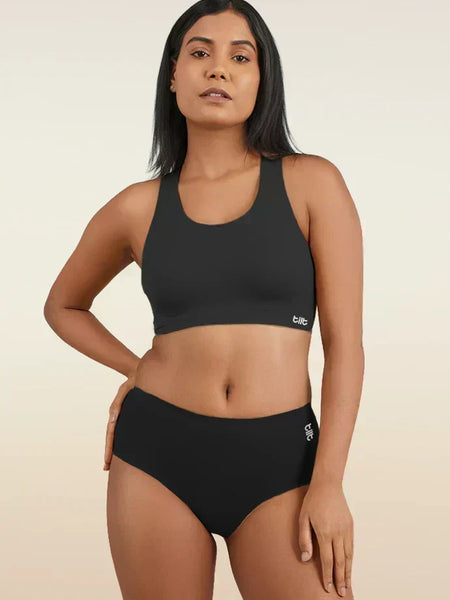 Woman wearing a black sports bra and mid-waist underwear on a beige background