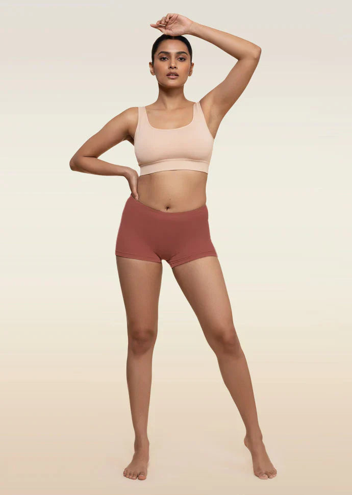Woman wearing a beige sports bra and red boyshorts on a beige background