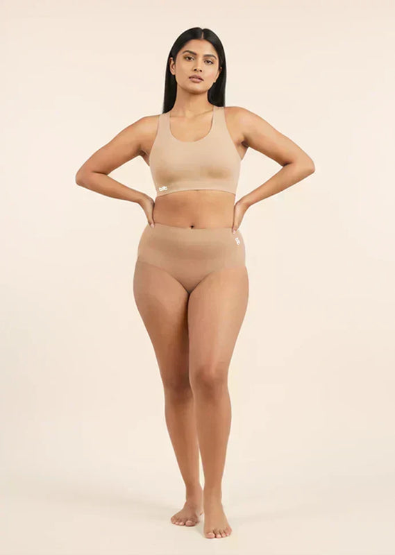 Woman wearing a beige sports bra and mid-waist underwear set on a beige background