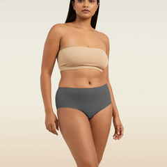 Woman wearing a beige strapless top and gray mid-waist underwear on a beige background