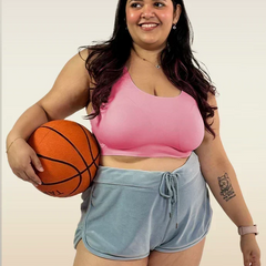 Woman holding a basketball wearing a pink bra and light blue shorts on a plain background
