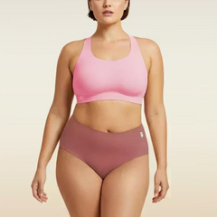 Woman wearing a pink sports bra and pink mid-waist underwear on a beige background
