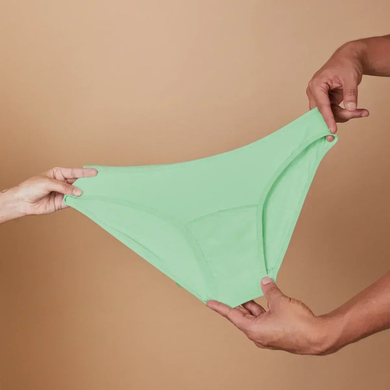 Green underwear held between two hands against a beige background