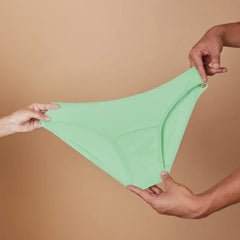Green underwear held between two hands against a beige background