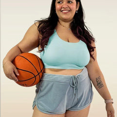 Woman holding a basketball wearing a  blue bra and gray shorts on a plain background
