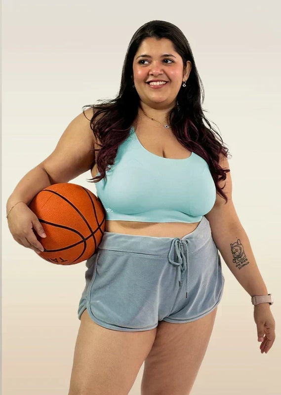 Woman holding a basketball wearing a  blue bra and gray shorts on a plain background