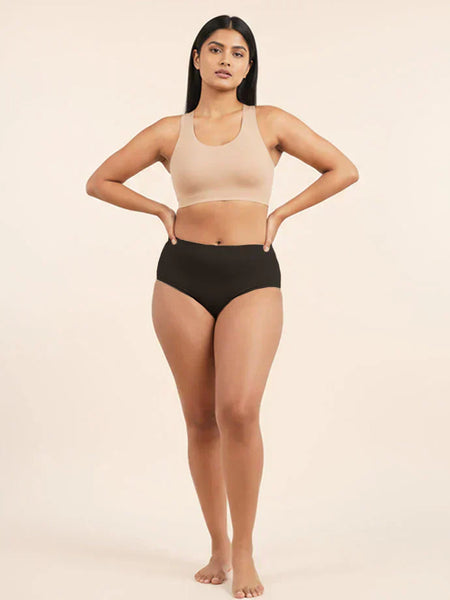 Woman wearing a beige sports bra and black mid-waist underwear on a beige background