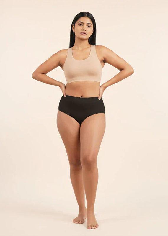 Woman wearing a beige sports bra and black mid-waist underwear on a beige background