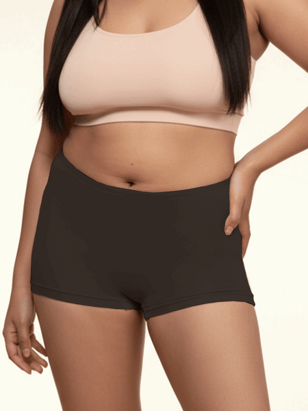 Person wearing a beige sports bra and black boyshorts on a beige background