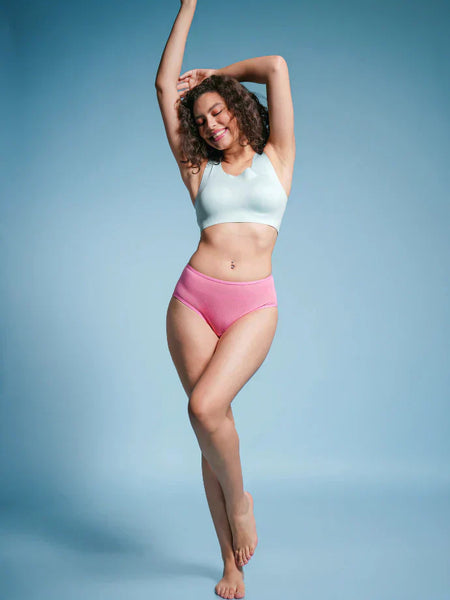 Woman wearing a light blue sports bra and pink mid-waist underwear against a blue background