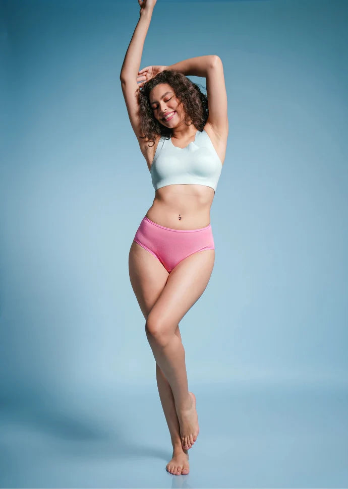 Woman wearing a light blue sports bra and pink mid-waist underwear against a blue background