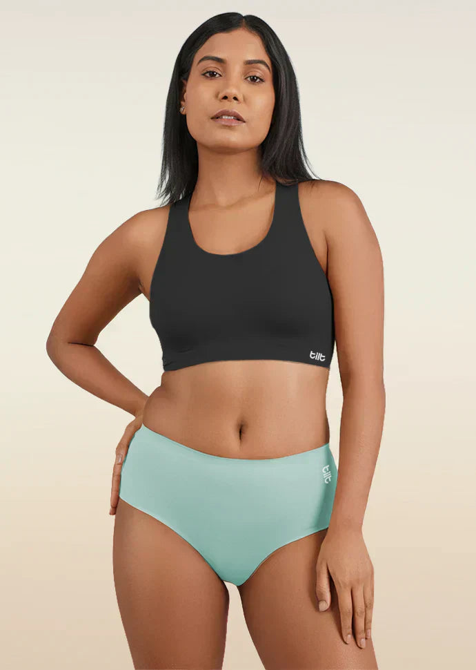 Woman wearing a black sports bra and  blue mid-waist underwear on a beige background