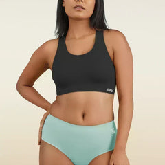 Woman wearing a black sports bra and  blue mid-waist underwear on a beige background