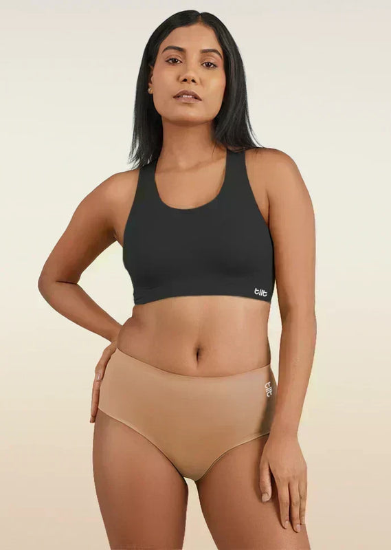 Woman wearing a black sports bra and beige mid-waist underwear on a beige background
