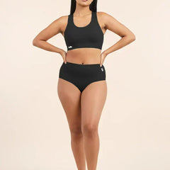 Woman wearing a black sports bra and  mid-waist underwear on a beige background