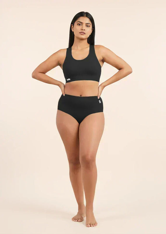 Woman wearing a black sports bra and  mid-waist underwear on a beige background