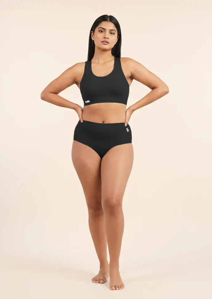 Woman wearing a black sports bra and  mid-waist underwear on a beige background