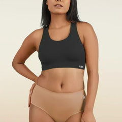 Woman wearing a black sports bra and beige mid-waist underwear on a beige background