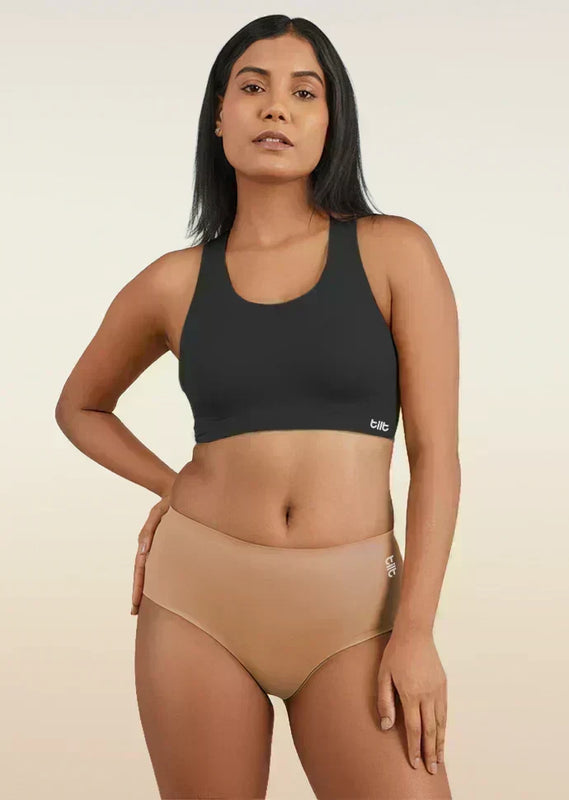 Woman wearing a black sports bra and beige mid-waist underwear on a beige background