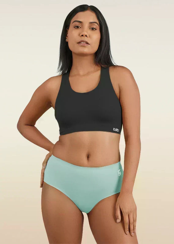 Woman wearing a black sports bra and  blue mid-waist underwear on a beige background