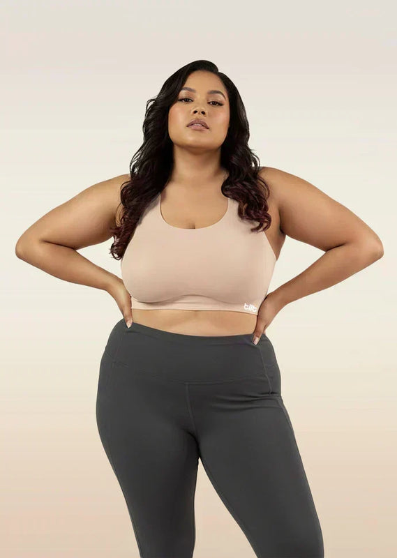 Woman wearing a beige sports bra and dark gray leggings on a beige background