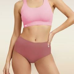 Woman wearing a pink sports bra and mid-waist pink underwear on a beige background