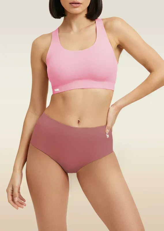 Woman wearing a pink sports bra and mid-waist pink underwear on a beige background