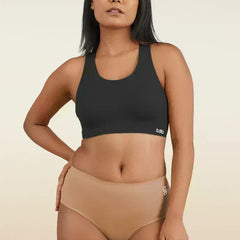 Woman wearing a black sports bra and beige mid-waist underwear on a beige background