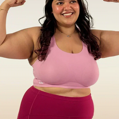Woman flexing her muscles wearing a pink sports bra and maroon leggings on a white background