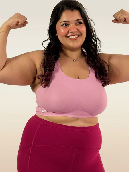 Woman flexing her muscles wearing a pink sports bra and maroon leggings on a white background
