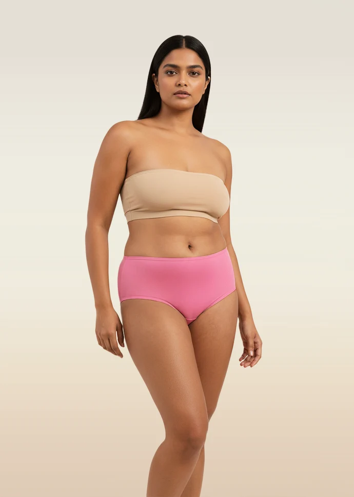 Woman wearing a beige strapless top and pink mid-waist underwear on a beige background