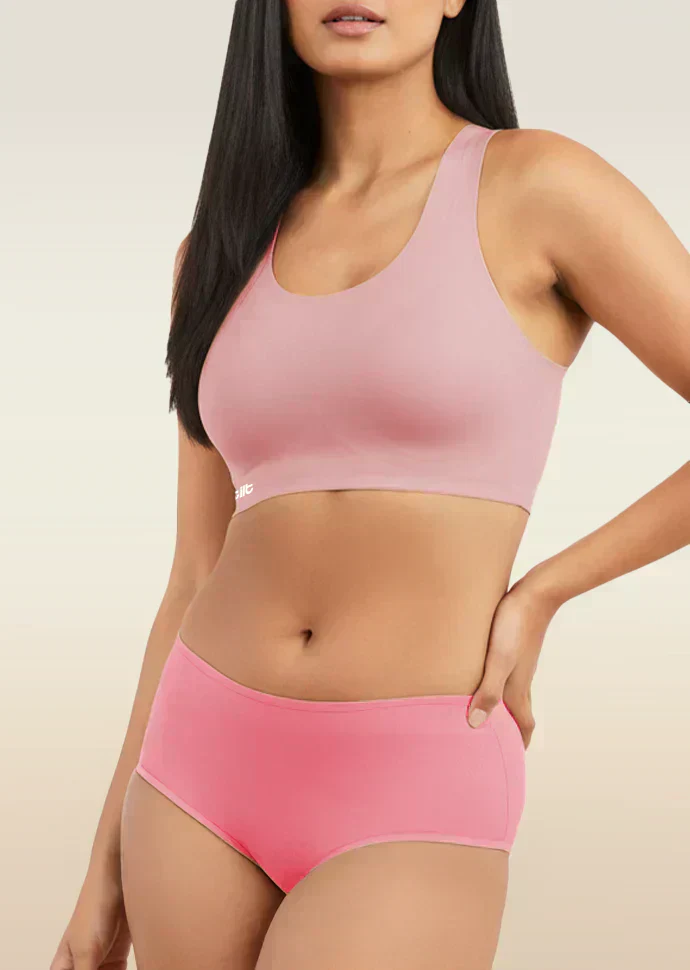 Woman wearing a pink sports bra and mid-waist underwear set on a beige background
