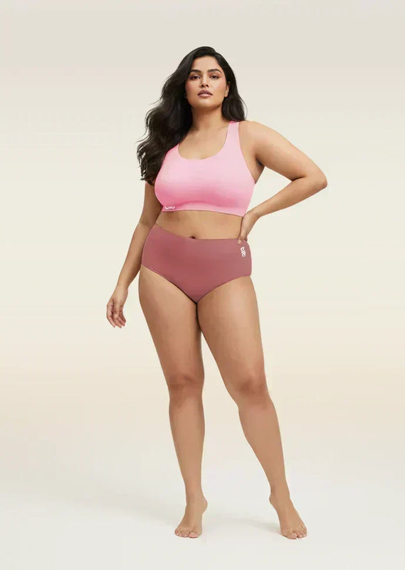 Woman wearing a pink sports bra and mid-waist underwear on a beige background