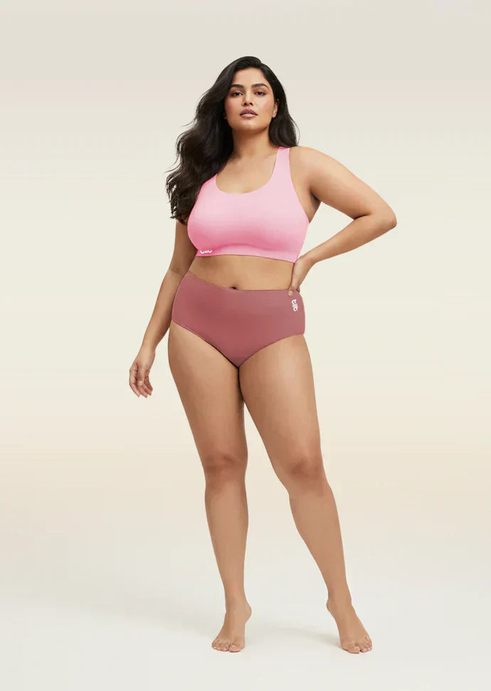 Woman wearing a pink sports bra and mid-waist underwear on a beige background