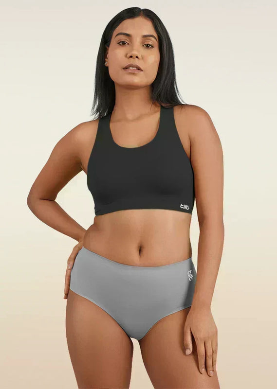Woman wearing a black sports bra and gray mid-waist underwear on a beige background