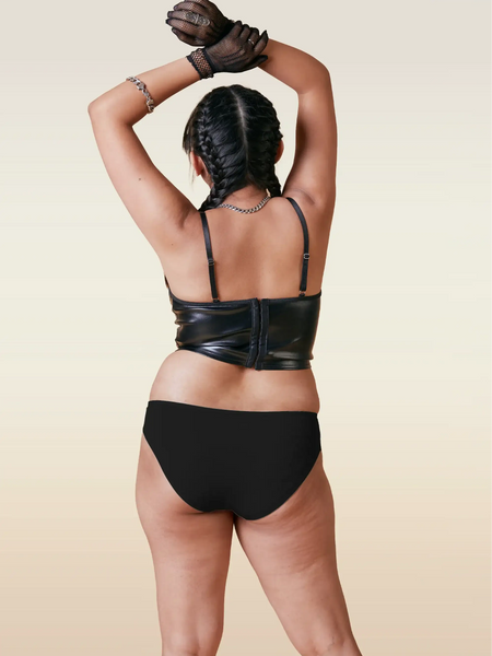 Person wearing a black leather top and underwear with a beige background