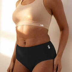 Person wearing a beige sports bra and black mid-waist underwear with 'tilt' branding.