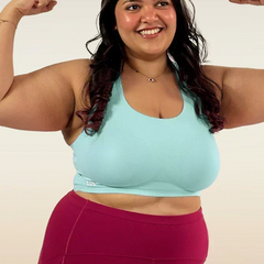 Woman flexing her muscles wearing a light blue bra and maroon leggings on a plain background