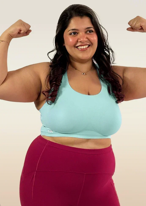 Woman flexing her muscles wearing a light blue bra and maroon leggings on a plain background