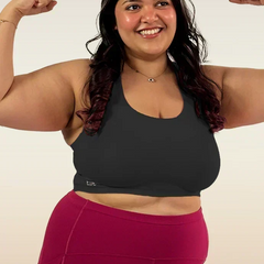 Woman flexing her muscles wearing a black sports bra and pink leggings on a white background