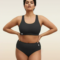 Woman wearing a black sports bra and mid-waist underwear on a beige background