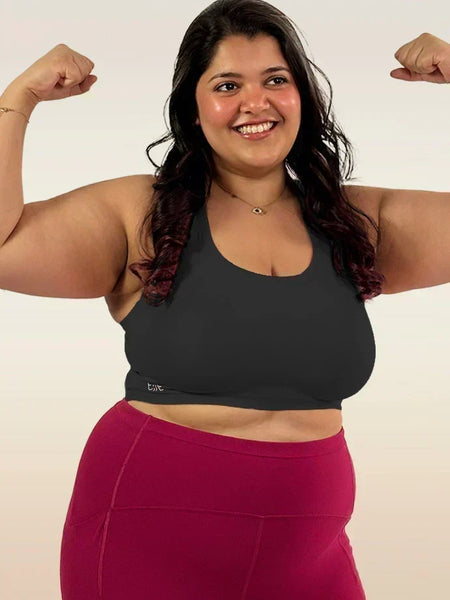 Woman flexing her muscles wearing a black sports bra and pink leggings on a white background